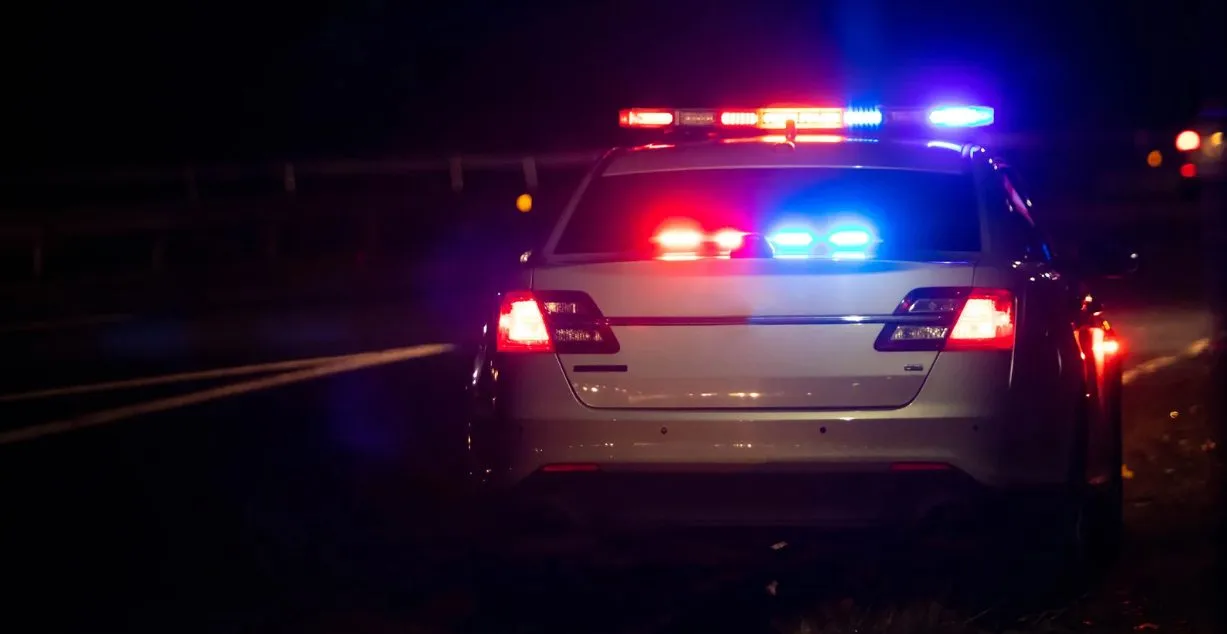(A police vehicle with flashing red and blue emergency lights patrolling at night.)