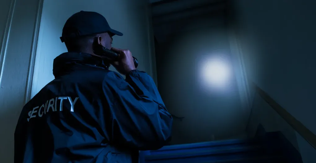 (A nighttime security guard patrols a dark stairwell with a flashlight, emphasizing the importance of vigilant 24/7 protection in low-light and high-risk areas.)