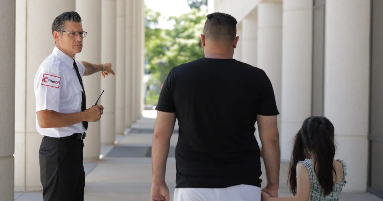 (A uniformed Citiguard security officer directs a man and his daughter outside a government or commercial building—showcasing approachable and professional private security services.)